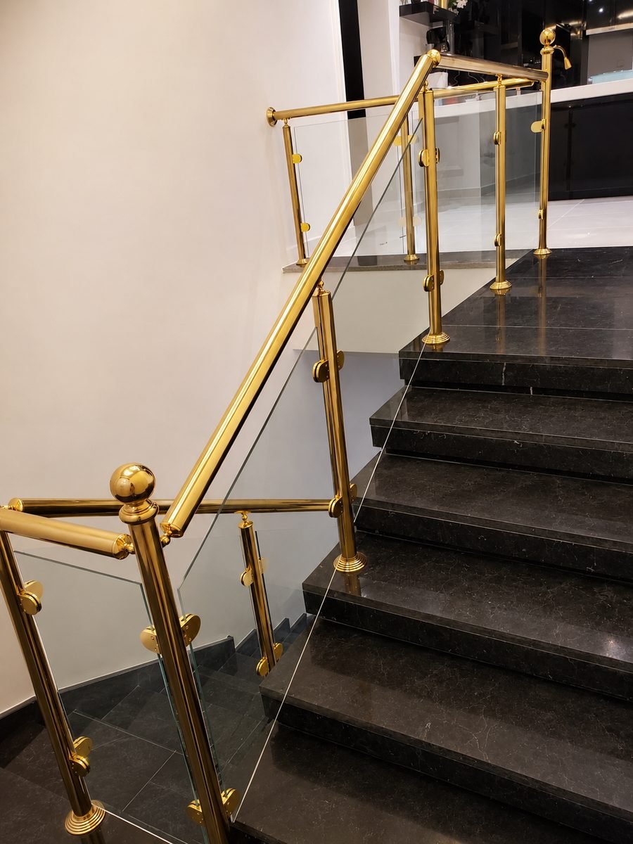 Polished brass posts and glass infill railing on a black marble staircase