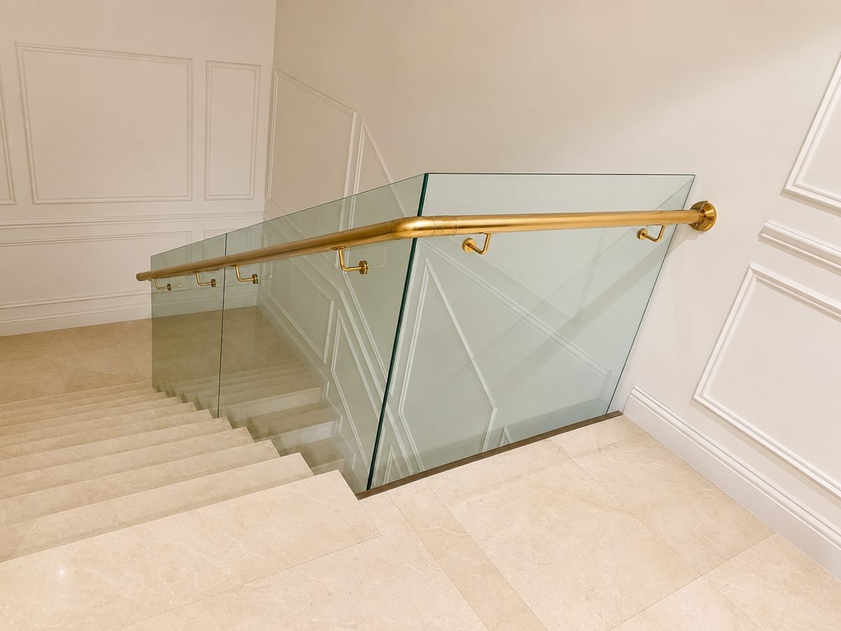 Frameless glass balustrade topped with a brushed brass handrail